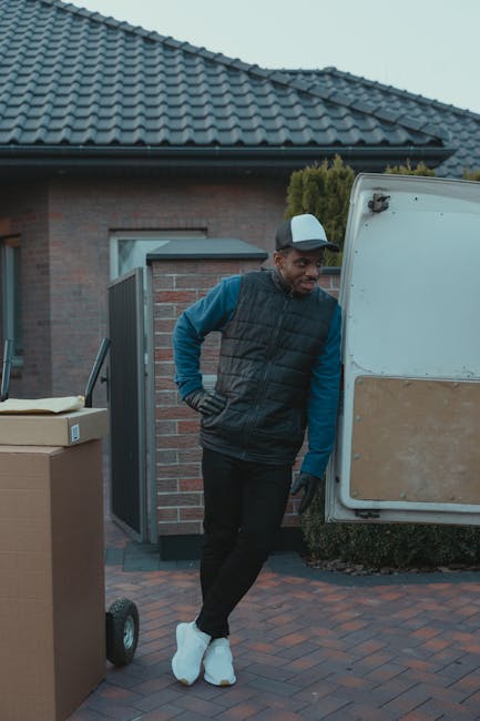 A person wearing a black cap is partially visible through the open driver's side door of a white delivery van, positioned on a paved street or parking area in UPMINSTER BRIDGE. The van's interior is n
