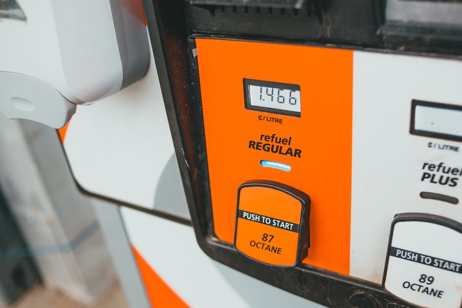 Close-up of a fuel pump display showing a total of 14.66 litres of petrol dispensed, with the fuel type labelled as 'refuel REGULAR'. The pump features an orange and white casing, with a digital screen and a black push-to-start button indicating 87 octane. Part of the fuel nozzle and hose are visible on the left side. The setting appears to be outdoors, near a vehicle loading or unloading area, relevant to the transportation aspect of home relocation and furniture transport. This image illustrates the fueling process involved in vehicle use for removals and moving services, as operated by Man with Van Upminster Bridge, supporting the topic of house removals and associated costs.